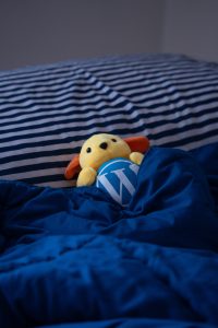 Wapuu(mascot of the WordPress open-source project) taking nap in a bed with a striped white and navy blue pillow in the background.