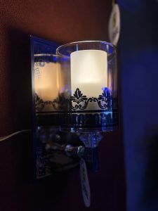 A decorative wall sconce with a frosted glass candle holder and black ornate details.
