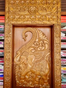 An intricately carved teak wooden panel featuring an elephant design is displayed in a textile shop in Coimbatore, Tamil Nadu, as an interior decoration, highlighting traditional craftsmanship. 