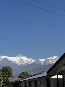 
A clear blue sky frames a majestic mountain range with snow-capped peaks. In the foreground, there are several buildings with a stone facade and a sloping roof.