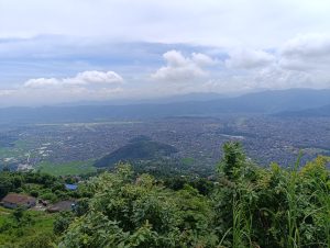 A panoramic view from a high vantage point overlooking a sprawling city surrounded by mountains.