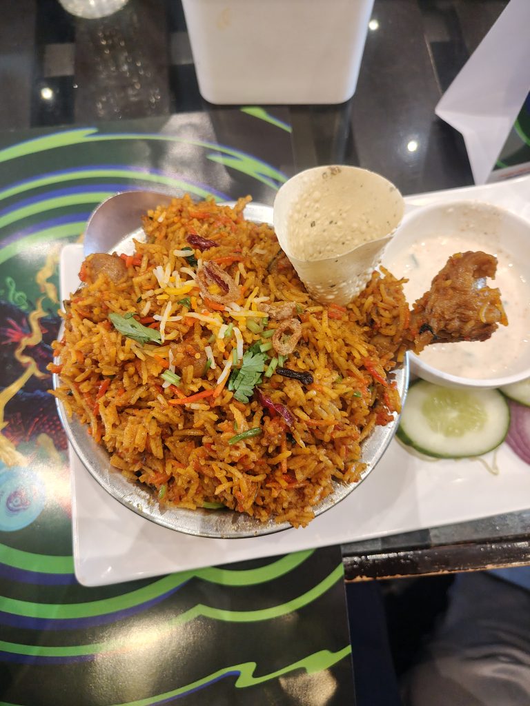 A bowl of biryani rice topped with coriander and garnishes is presented on a table.