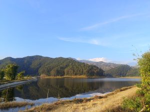 
A serene landscape featuring a calm lake reflecting the surrounding mountains and clear blue sky.