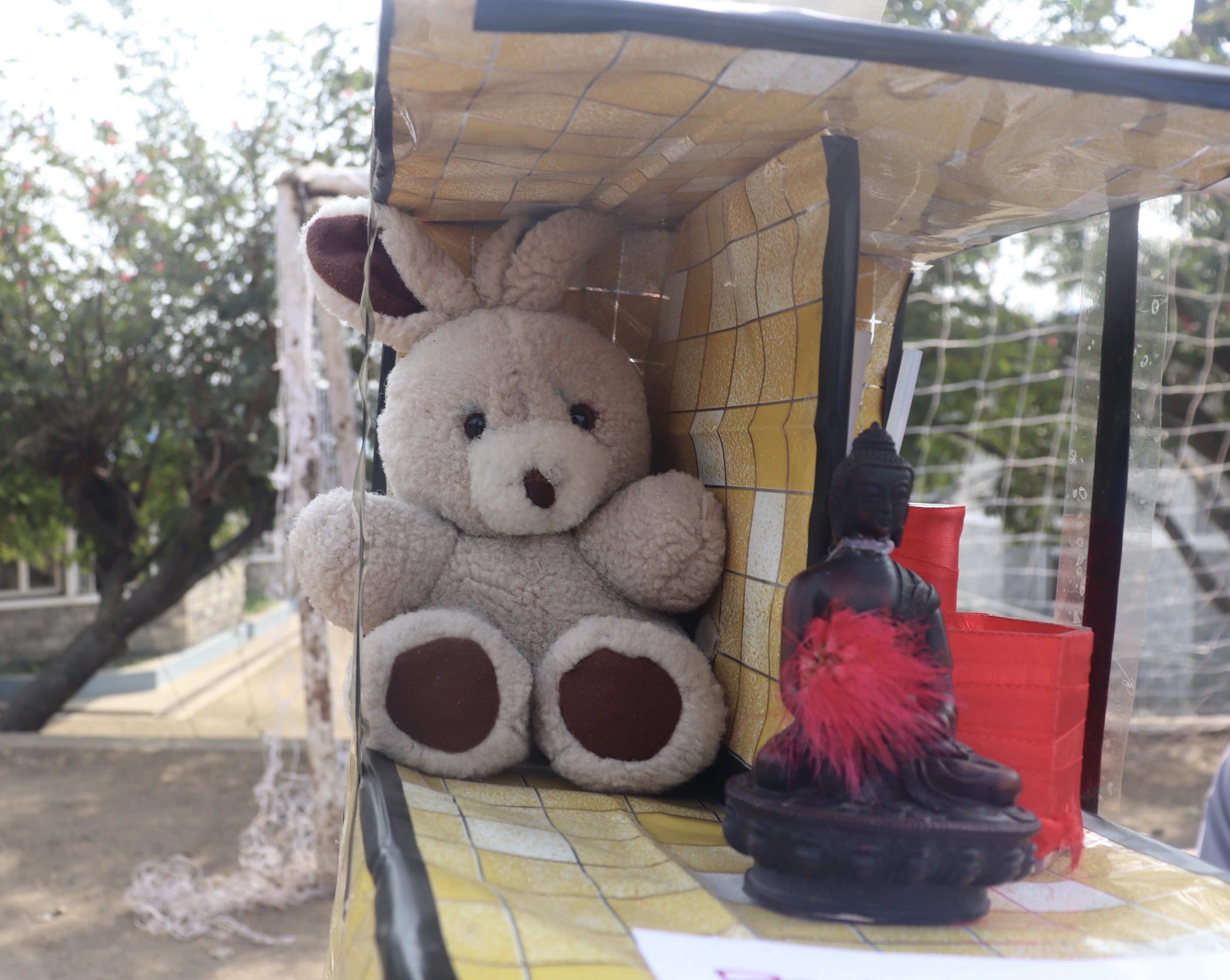A soft plush bunny sits next to a small black statue of Buddha on a yellow checkered surfac