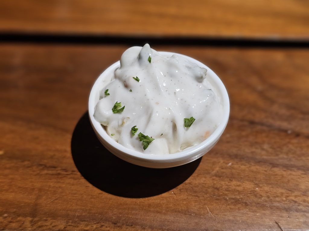 A small bowl of creamy white dip garnished with herbs sits on a wooden table in Kozhikode, Kerala, looking smooth, fresh, and ready to serve.