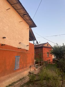 A colorful village scene featuring two houses painted in orange and cream, with wooden support beams visible.