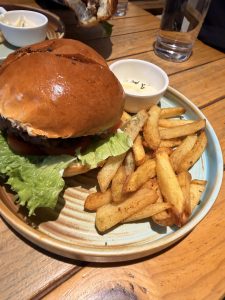 A hamburger with fries and dipping sauce on a blue plate, served on a wooden table with a glass of water in the background.