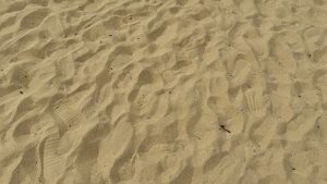 A close-up view of golden beach sand covered in numerous overlapping footprints and small indentations.