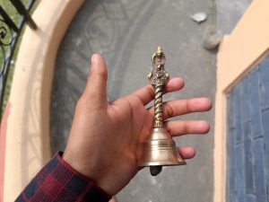 
A hand holding a small brass bell with intricate designs on the handle.