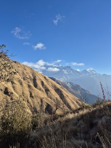 
A panoramic view of a mountainous landscape featuring sloping hills covered with dry grass and sparse vegetation in the foreground.