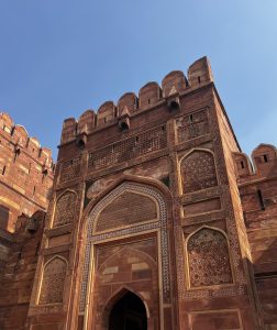 A close-up view of a red sandstone fort featuring intricate carvings and a large, ornate archway. 