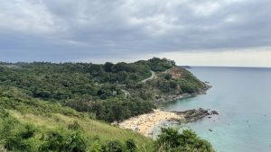 A high-angle, wide view of a beautiful sandy beach nestled in a cove between rocky, lush green headlands under a cloudy sky.