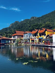 A calm lakeside view with colorful red and yellow buildings reflected in the water.