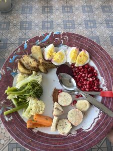 A plate with roasted potatoes, halved boiled eggs, pomegranate seeds, and mixed vegetables like broccoli, cauliflower, and carrots.