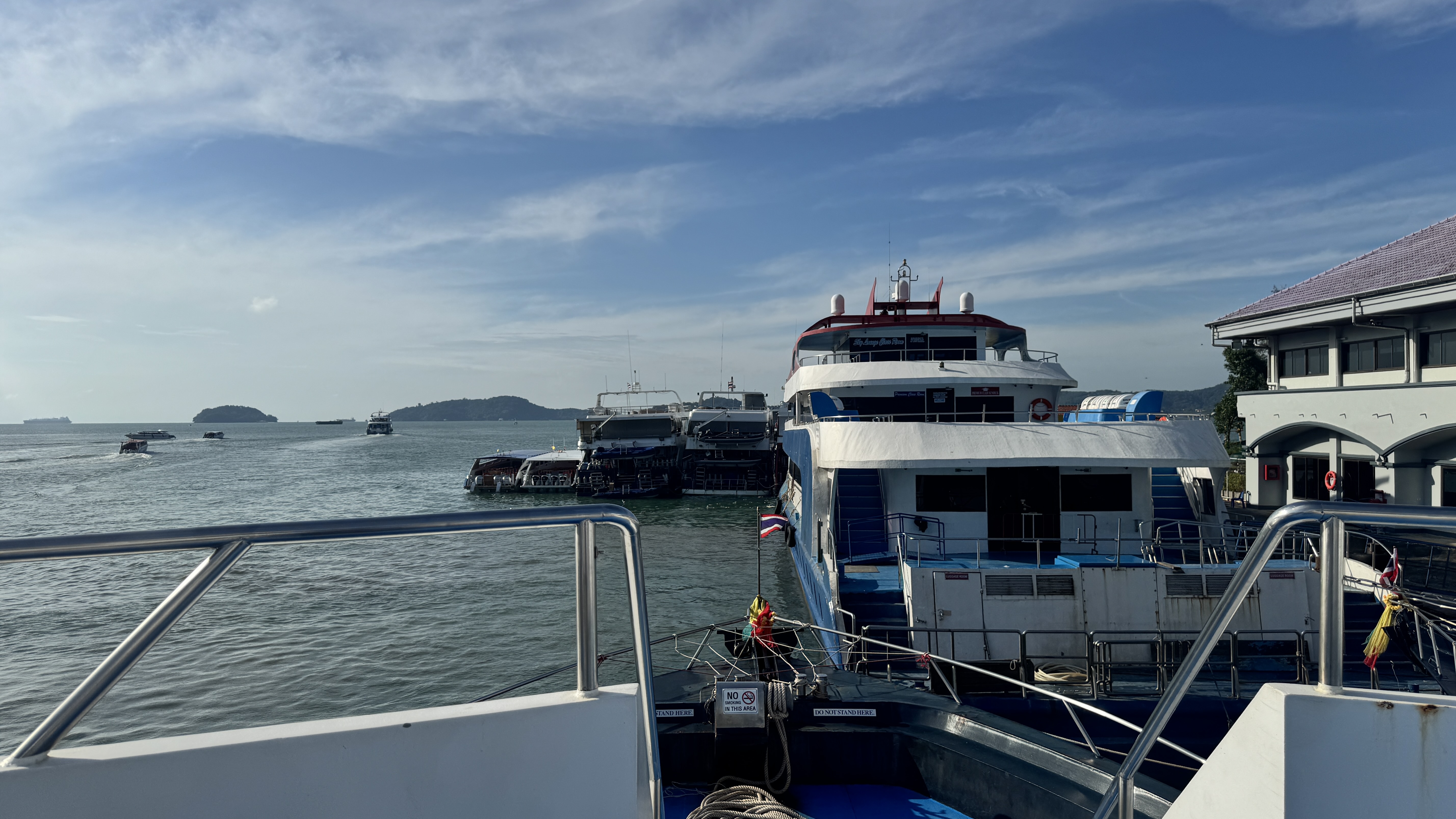 A view from the front of a passenger ferry looking toward several other ferries docked at a pier under a blue sky.