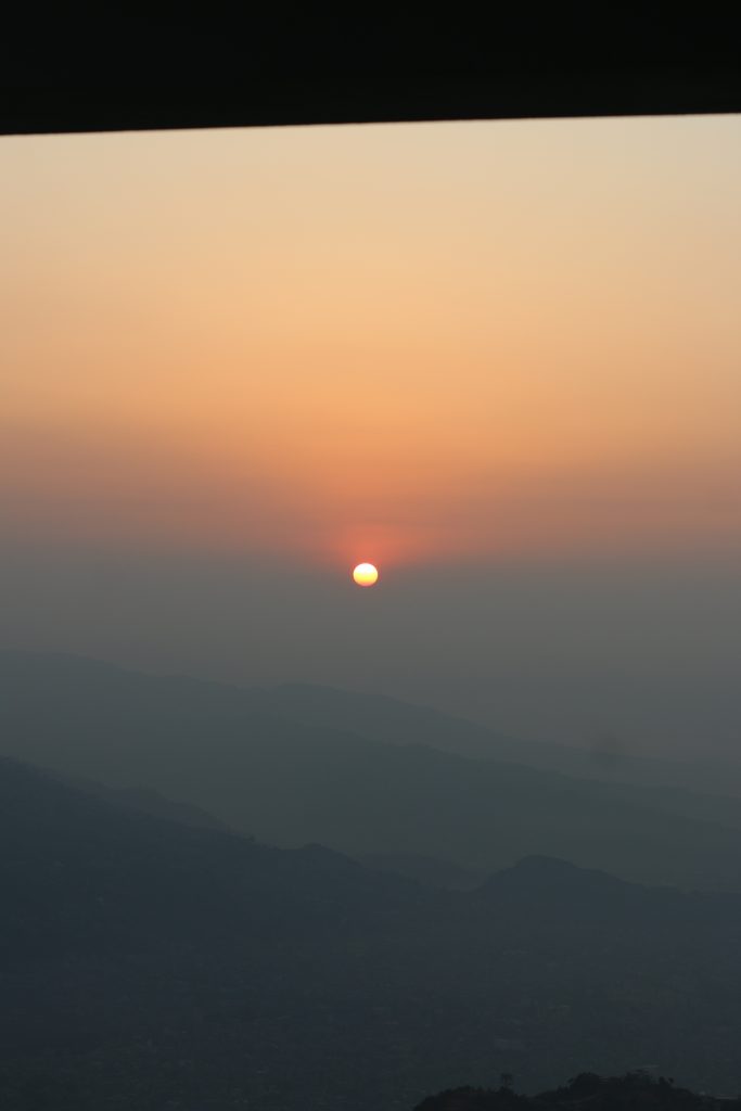 A serene sunrise over a mountainous landscape, with a warm orange and pink sky.