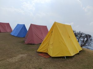 Colorful camping tents—yellow, red, and blue—pitched on a grassy hill under a cloudy sky