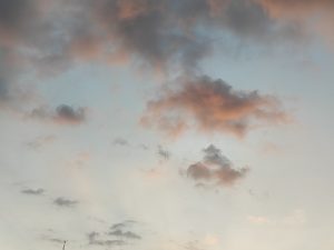 A serene sky filled with soft, fluffy clouds in various shades of gray and pink, against a backdrop of pale blue.
