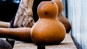A close-up shot of a traditional Ugandan calabash gourd with a smooth, earthy brown texture, resting on a rustic wooden surface alongside other carved wooden items in a soft-focus background.