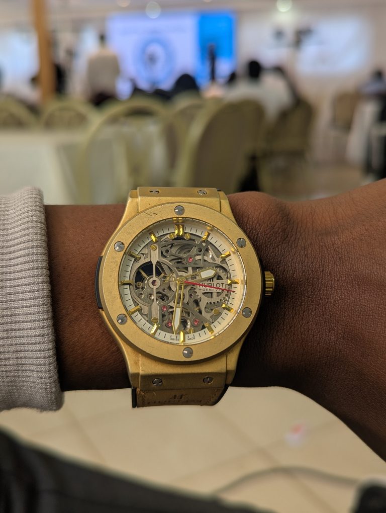 A close-up of a wrist wearing a luxurious gold watch with a transparent dial showing its intricate gears.