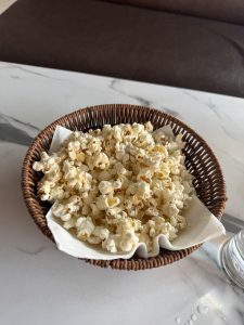 
A woven brown basket filled with freshly popped popcorn is resting on a marble table