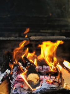 Close-up of burning logs with bright flames, turning into ash and glowing embers in a fireplace.