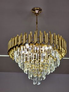 An elegant golden chandelier with sparkling crystal drops hanging from the ceiling. The bright lights and detailed design create a luxurious look in this indoor scene from S.M.Street, Kozhikode.
