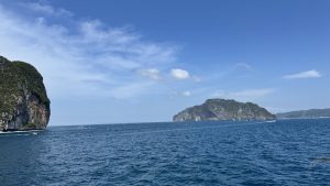 A wide landscape shot showing several large, forested limestone mountains and islands rising from the calm blue sea.