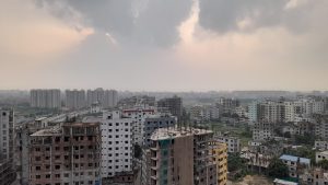 Urban city view with mid-rise apartments and construction sites under a cloudy sky, with sunlight breaking through over a dense residential area.