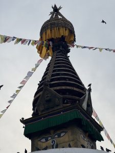 Ornate upper section of a stupa with a golden dome and intricately carved tiered roofs.
