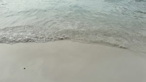 A close-up of soft sea foam from small waves rolling onto a pristine white sand beach.