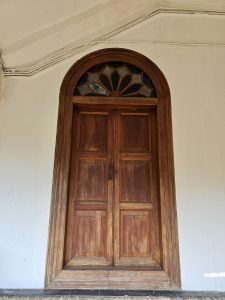 A classic wooden door with a decorative glass arch above, showing rich textures and traditional design. A timeless architectural detail from Kozhikode, Kerala.