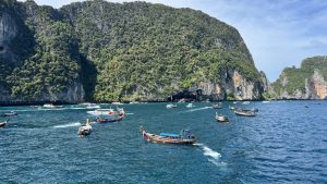 Tourists on the deck of a boat looking out at a stunning panoramic view of massive limestone islands and turquoise water under a bright blue sky.