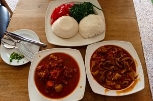 Top-down view of posho, greens, kachumbari, and two bowls of stew served on a wooden table.