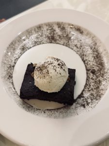 A slice of chocolate cake topped with a scoop of vanilla ice cream, presented on a white plate.