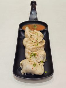 Steamed dumplings (momos) served in a black dish with spicy dipping sauce. The soft texture and simple presentation make the dish look delicious in this photo taken in Mavoor Road, Kozhikode.

