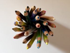 A top-down view of sharpened colored pencils in a radial bundle, forming a bright starburst on a clean white background.