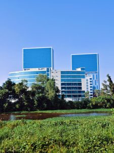 A modern architectural structure featuring two tall, glass-covered buildings with blue reflective surfaces, situated behind a lower building with large glass windows.