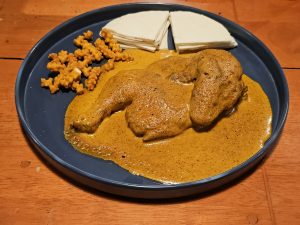 A plate of rich chicken curry (Masala Shawaya) served with crispy snacks and flatbread slices. The warm colors and textures show a delicious restaurant meal in Palazhi, Kozhikode, Kerala.
