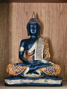 A detailed Buddha statue in black and gold tones, placed against a wooden background. A calm and artistic composition captured in Kozhikode, Kerala.