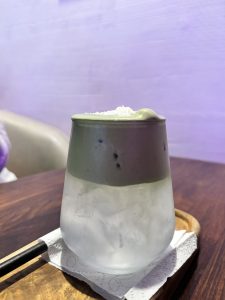 A glass cup of iced matcha tea with layered green and purple colors.