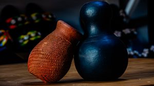 A smooth, matte-black, gourd-shaped vessel stands upright beside a smaller reddish-brown terracotta pot with a rough, pitted texture, both resting on a wooden tabletop.