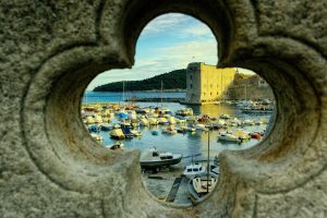 The image is captured through a clover-shaped stone opening, likely part of a medieval wall. This "frame within a frame" technique creates a beautiful sense of depth and focus, drawing the eye directly to the vibrant scene outside.