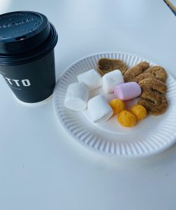 Black coffee cup with snacks on a white plate, on a white surface.
