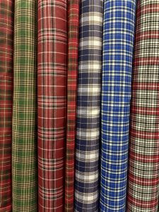 A selection of rolled fabrics featuring various plaid patterns in colors such as green, red, brown, blue, and navy, arranged side by side