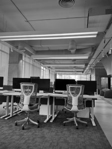 A modern office space featuring several white desks with computer monitors and ergonomic chairs.
