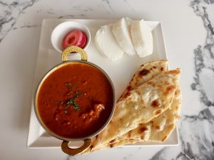 Top-down view of an Indian-style meal on a white square plate with mutton rogan josh, naan bread, white posho, and pickled red onions.