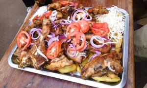 Large tray with grilled chicken, potato chips, and fresh salad on a rustic wooden table