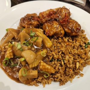 A plated meal featuring three pieces of golden-brown chicken, garnished with red threads, alongside a serving of brown rice speckled with herbs.