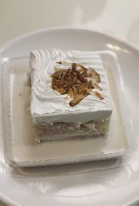 A square piece of cake on a white plate, showcasing its layers and frosting.